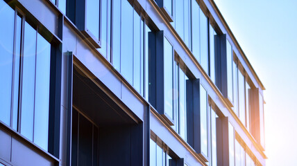 Obraz premium Modern glass building and rising sun. Glass facade on a bright sunny day with sunbeams in the blue sky. Economy, finances, business activity concept. 