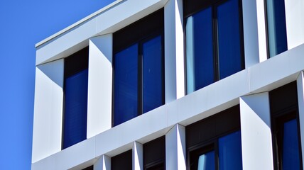 Fragment of a modern white office building. Facade of modern building. Reflection of sky in windows. Abstract blue architectural background.