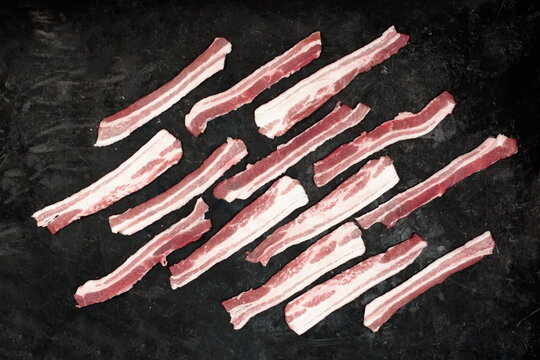 Cold Sliced Bacon On Black Table Grunge Background, Overhead View. Streaky Fresh Bacon Top View.