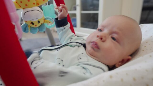 2 month old baby boy in bouncer for babies, infant playing with hanging toys. High quality 4k footage