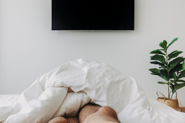 Fototapeta na wymiar Person sleeping on white bed and watching television. Concept of stay at home.