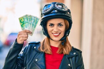 Young latin woman wearing motorcycle helmet holding israel shekels banknotes at the city.