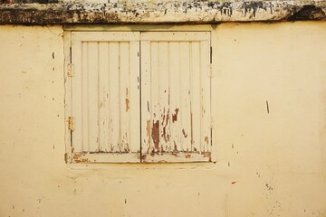Pair of closed wooden shutters off center in faded yellow painted wall