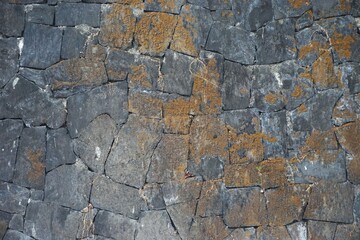 Stone tile mosaic with tightly fitted angles and orange lichen patches on the surface