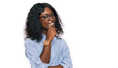 Fototapeta na wymiar Beautiful african young woman wearing casual clothes and glasses looking confident at the camera smiling with crossed arms and hand raised on chin. thinking positive.