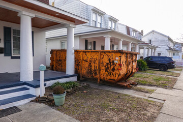 An old yellow scraped up dumpster in a driveway between two very close houses