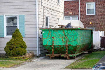 The end of an old blue green dumpster filled with construction debris in a driveway between two...
