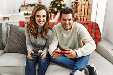 Young hispanic couple smiling happy sitting on the sofa playing video game at home.