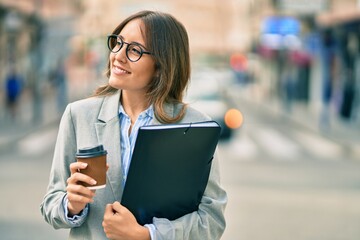 Young hispanic businesswoman drinking coffee holding binder at the city.