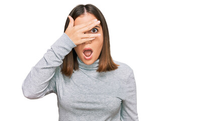 Young beautiful woman wearing casual turtleneck sweater peeking in shock covering face and eyes with hand, looking through fingers with embarrassed expression.