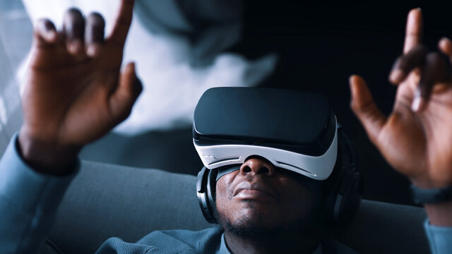 African-American man wearing virtual reality glasses and headset lying on the sofa. Touching the air. Futuristic. High quality photo