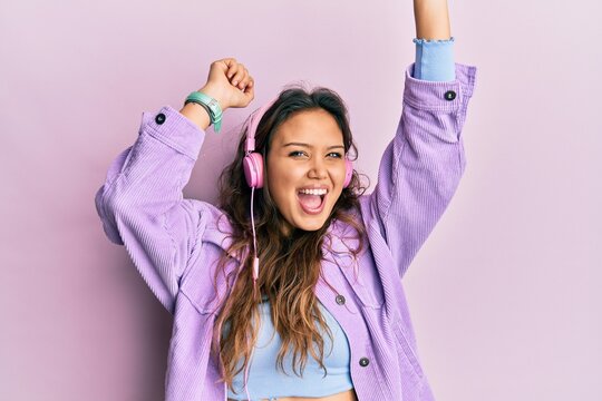 Young hispanic girl dancing and listening to music using headphones celebrating crazy and amazed for success with open eyes screaming excited.