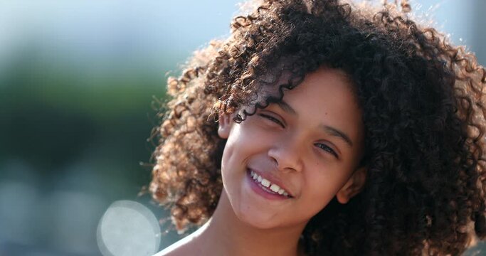 Black preteen girl child smiling at camera standing outside. African kid with curly hair