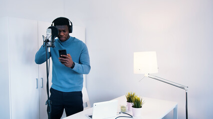 Man wearing headphones singing a song into a microphone in a studio. Holding a phone in his hand...