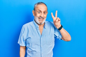 Handsome senior man with beard wearing casual blue shirt smiling with happy face winking at the...
