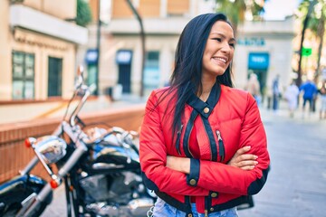Young latin woman smiling happy standing over motorcycle at the city.