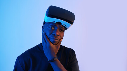 African-American guy with virtual reality glasses on his forehead looking around. Thinking something. Virtual headset glasses. Blue background. Studio footage. . High quality photo