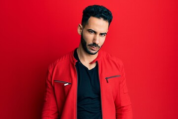 Fototapeta premium Young hispanic man wearing red leather jacket skeptic and nervous, frowning upset because of problem. negative person.