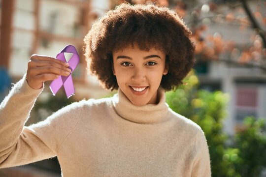 Young hispanic girl smiling happy holding purple awareness ribbon at the city.
