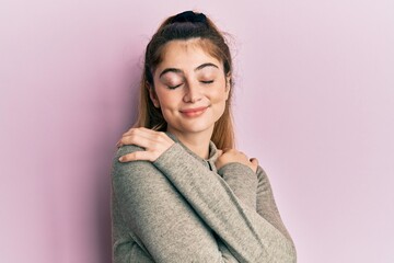 Fototapeta premium Young caucasian woman wearing casual clothes hugging oneself happy and positive, smiling confident. self love and self care