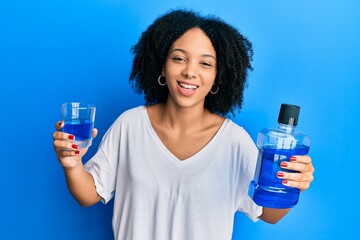 Young african american girl holding mouthwash for fresh breath smiling and laughing hard out loud...