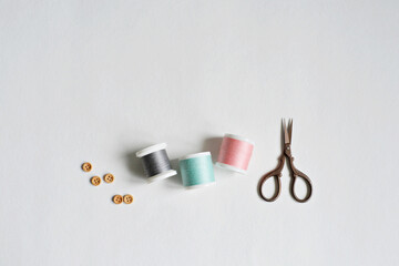 Spool threads, wooden buttons and small scissors on white background