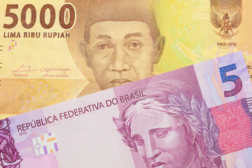 A macro image of a pink and purple five real bank note from Brazil paired up with a orange five thousand Indonesian rupiah note.  Shot close up in macro.