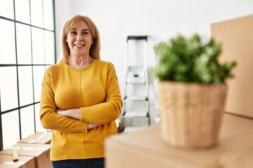 Middle age blonde woman standing with arms crossed gesture at new home.