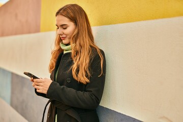 Young blonde girl smiling happy using smartphone at the city.