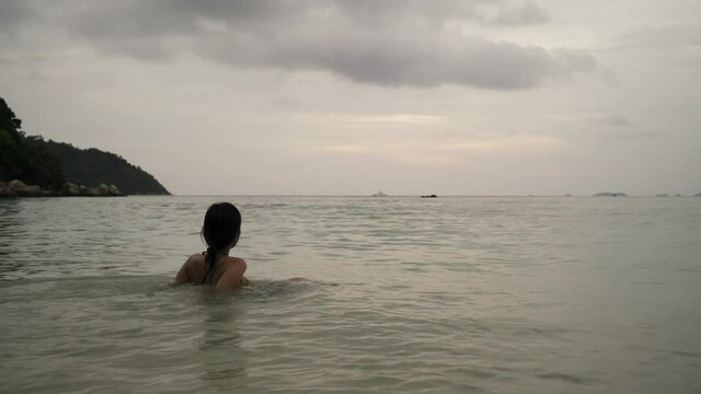 Asian women sitting on the beach and looking toward the sky at sunset