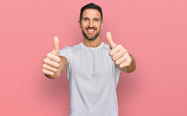 Handsome man with beard wearing casual white t shirt approving doing positive gesture with hand, thumbs up smiling and happy for success. winner gesture.