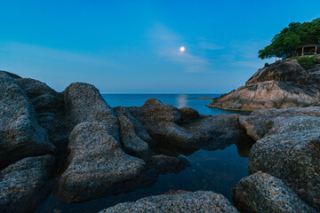 Fototapeta na wymiar Full moon in the sunset sky over the rocks and sea