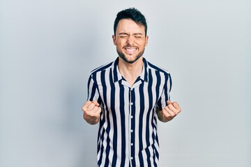 Fototapeta premium Young hispanic man wearing casual clothes very happy and excited doing winner gesture with arms raised, smiling and screaming for success. celebration concept.