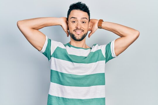 Young hispanic man wearing casual clothes relaxing and stretching, arms and hands behind head and neck smiling happy