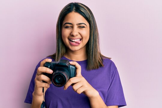 Young latin woman using reflex camera sticking tongue out happy with funny expression.