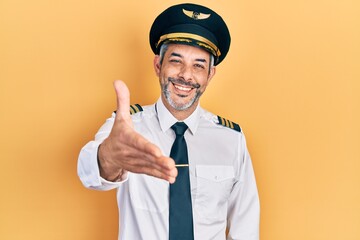 Handsome middle age man with grey hair wearing airplane pilot uniform smiling friendly offering handshake as greeting and welcoming. successful business. - obrazy, fototapety, plakaty