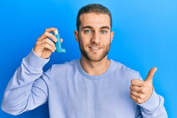 Young caucasian man holding medical asthma inhaler smiling happy and positive, thumb up doing...