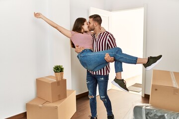 Young caucasian man holding woman in arms gettin in new home door.