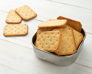 Cracker cookies in a stainless steel bowl on white wooden table background.