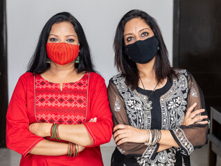 Portrait of two Indian women standing together wearing Covid 19 protection mask and with arms crossed.