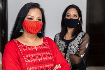 Portrait of two Indian women standing together wearing Covid 19 protection mask and with arms crossed.