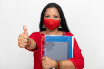 Portrait of an Indian woman showing her thumb as sign of success and approval, female holding files and folders, woman wearing Covid 19 protection.