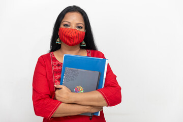 Portrait of an Indian woman standing against white wall,, female holding files and folders, woman wearing Covid 19 protection mask.