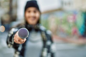 Young hispanic woman smiling happy using headphones and microphone at the city.