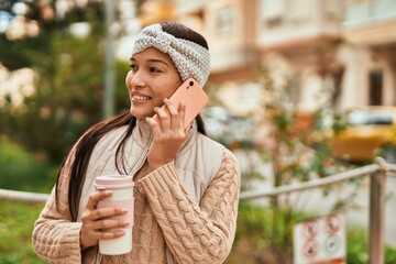 Young latin woman talking on the smartphone drinking coffee at the city.