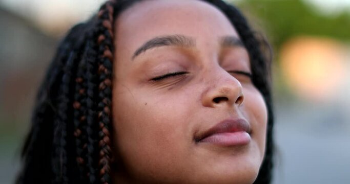Black preteen girl closing eyes in contemplation. Child opening eye to sky smiling