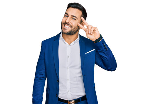 Young hispanic man wearing business jacket doing peace symbol with fingers over face, smiling cheerful showing victory