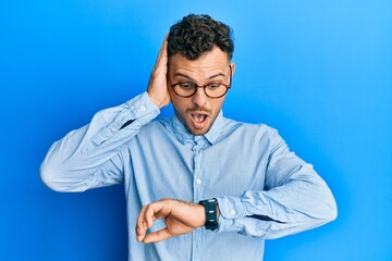 Young hispanic man wearing casual clothes and glasses looking at the watch time worried, afraid of...