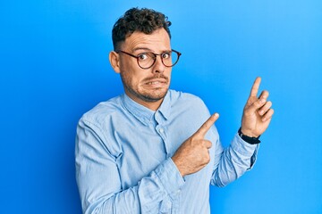 Naklejka premium Young hispanic man wearing casual clothes and glasses pointing aside worried and nervous with both hands, concerned and surprised expression