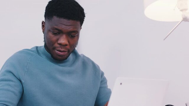 African American black man sitting at the table in front of a laptop and using a smartphone with a smile. Remote work concept. High quality 4k footage